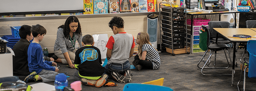 Student teacher sitting on the floor with five children