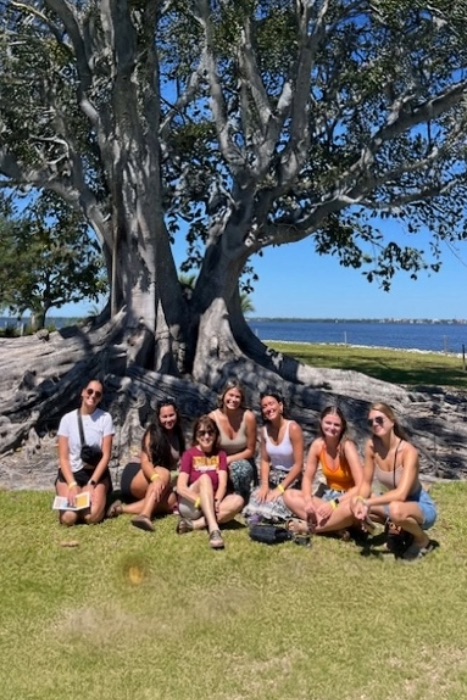 Students sitting in the grass in front of a very large tree in Florida.