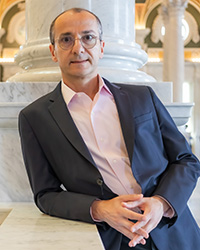Khatchig Mouradian wearing a suit and leaning against a decorative marble wall.