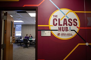 Image of two people seated at a table seen through the doorway of the CLASS Hub