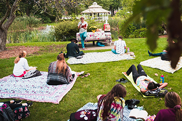 Students and faculty sit on blankets in the grass reading from Walt Whitman's Leaves of Grass.