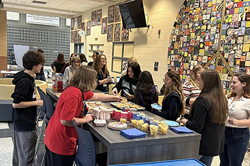 Mount Pleasant High School and Central Michigan University students stand around a table filled with breakfast foods.