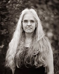 Closeup image of Joanna White wearing a black shirt and standing near trees.