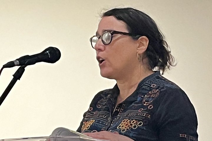 Helena Mesa stands facing a microphone to read from her book.