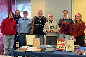 Jett Whitehead holds a book and stands behind a table filled with rare books while students stand on either side of him.