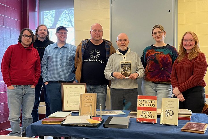 Jett Whitehead holds a book and stands behind a table filled with rare books while students stand on either side of him.