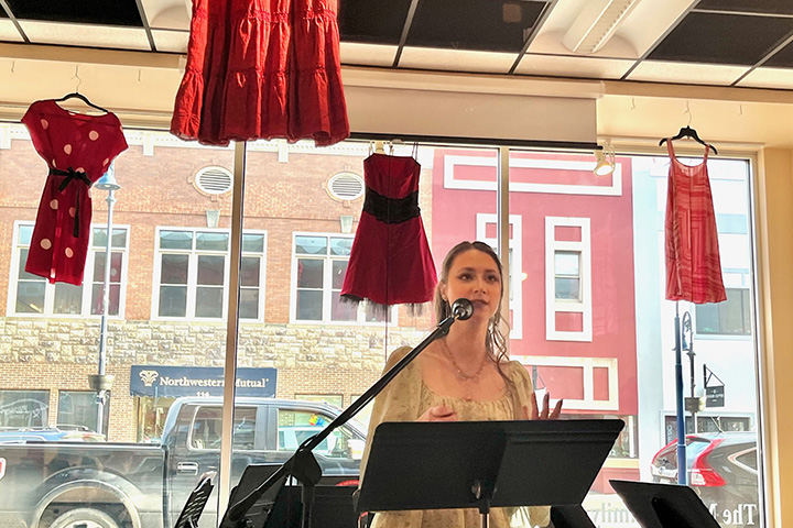 Central Michigan University student Brenna Dean reads her poetry while standing in front of a large glass window at Art Reach of Mid Michigan