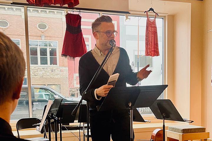 Robert Fanning speaks into a microphone while standing in front of a large glass window at Art Reach of Mid Michigan
