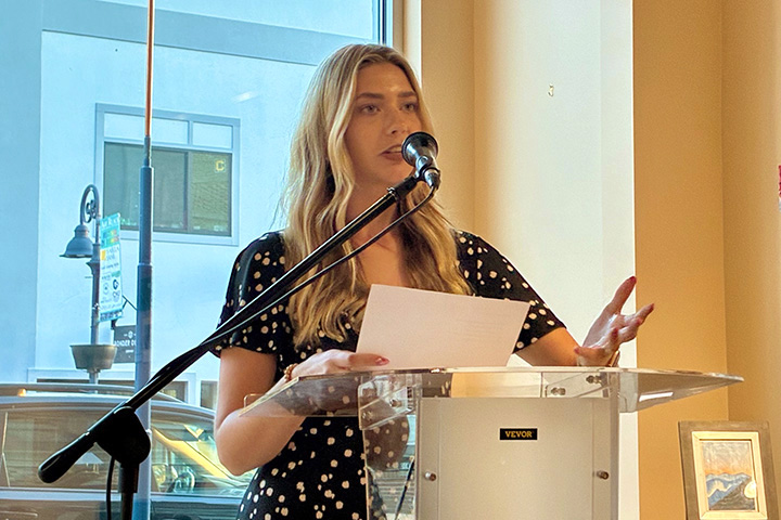 Wellspring Literary Series featured student reader Autry Clark stands at a podium while speaking into a microphone and holding a piece of white paper..