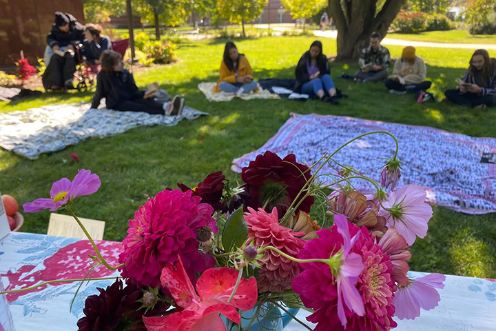 Flowers decorate a table while guests sit on blankets reading Walt Whitman's Leaves of Grass during an annual marathon reading.