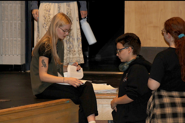 McKenzie Gerstenberger flips through a stack of papers while seated on a stage with students waiting in line in front of her.