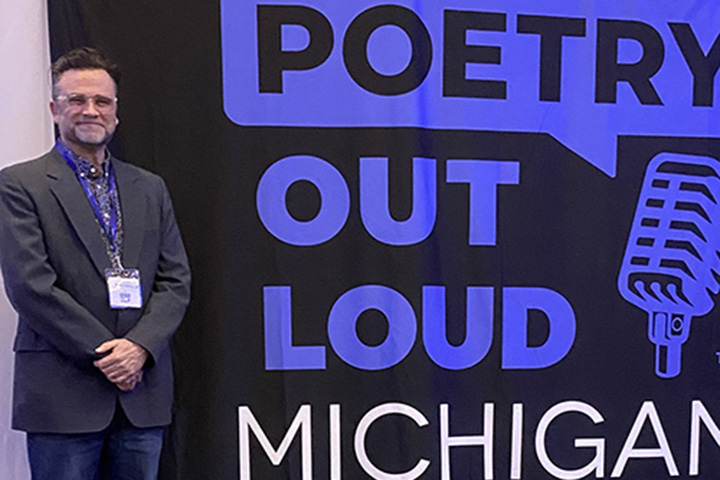 Robert Fanning stands next to a large banner that says Poetry Out Loud Michigan