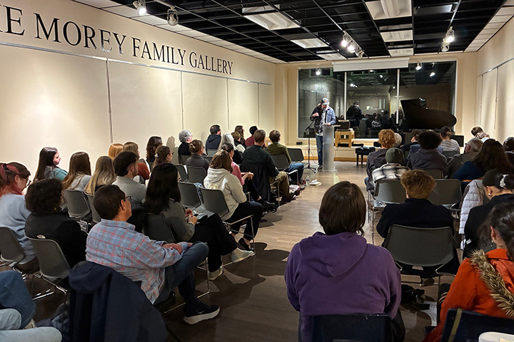 Call Freeman stands reading his poetry at a podium in front of rows of chairs filled with guests.