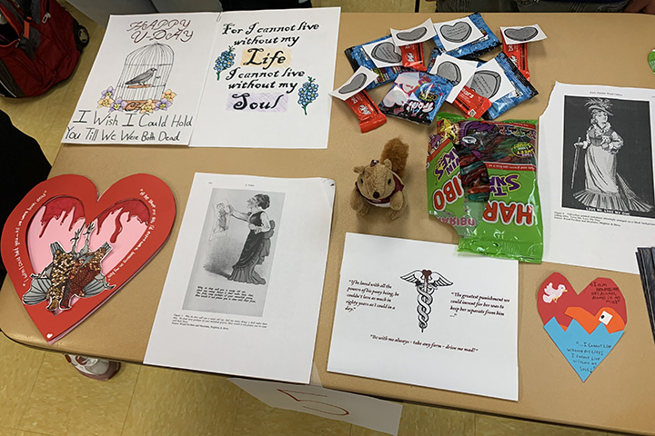 Student-designed bookmarks, Valentine's, candy and a small stuffed squirrel are displayed on desks in a classroom.
