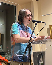 Dominic Tatrai reads poetry while standing at a podium with a microphone.