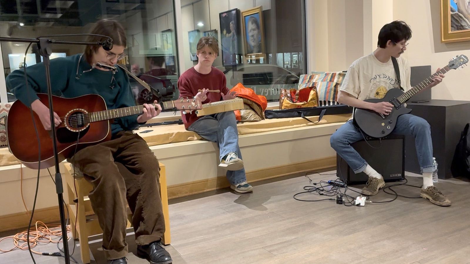 Three members of the band Well Done, Tim sit near a window holding instruments.