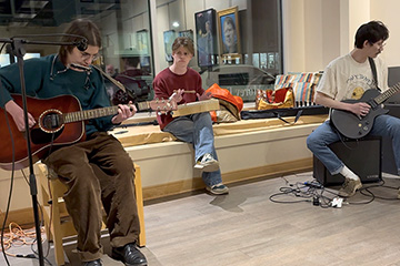 Three members of the band Well Done, Tim sit near a window holding instruments.