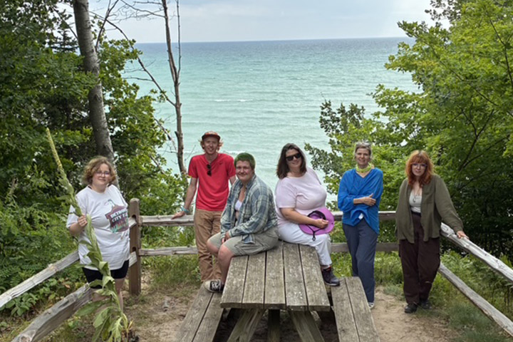 Students sit and stand near a picnic table with a view of Lake Michigan behind them.