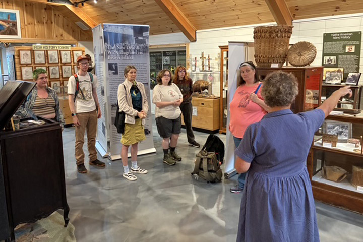 Students stand inside the Beaver Island Museum near posters, photographs and glass display cases.