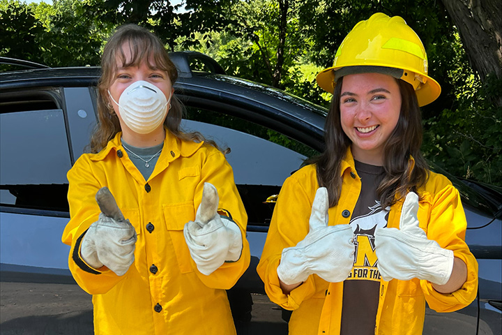 Image of Jane Amstutz left and another woman wearing yellow uniforms and white gloves giving a thumbs up sign