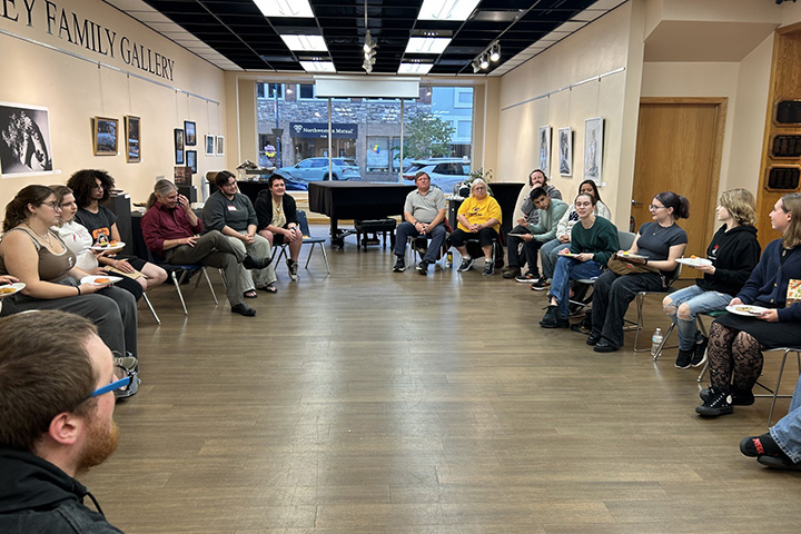 Individuals attending Desserts and Discourse sit in chairs in a circle facing each other.