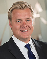 Closeup image of Frank Foster wearing a dark suit jacket and blue tie.