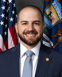 Closeup image of State Senator Jeremy Moss wearing a dark suit jacket and light blue tie.