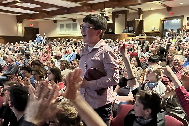 A large crowd seated in Plachta Auditorium during Michigan History Day while one student stands and others applaud and point at him