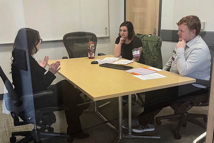A Michigan History Day participant presents a paper to two judges while seated and facing each other at a table..