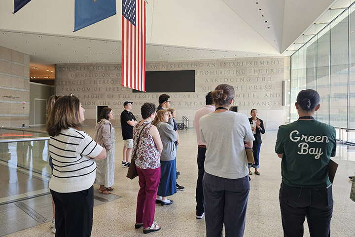 A group of individuals stand facing tour guide Sarah Harris at the National Constitution Center