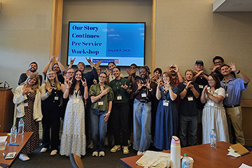 Social Studies education students stand in two rows in front of a television screen that says "Our Story Continues - Pre Service Workshop"