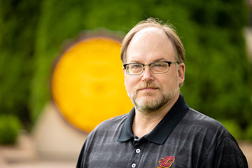 Ron Bloomfield stands in front of the Central Michigan University seal wearing a CMU shirt