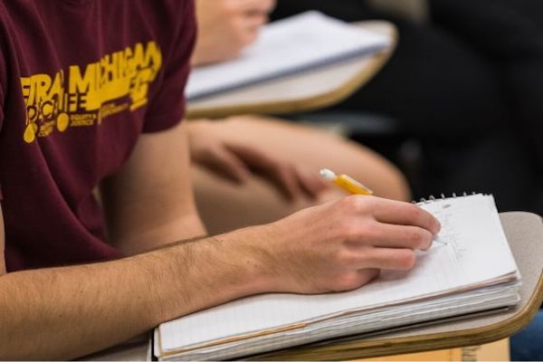 A student sitting at a desk and writing in a notebook.