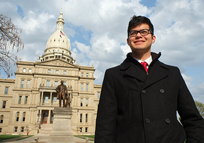 Student stands in front of the Michigan Capitol Building.