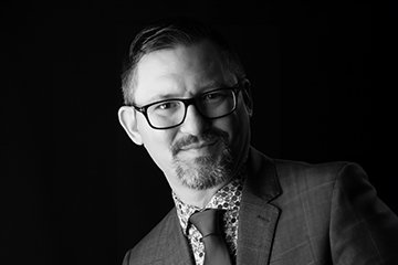 Closeup black and white image of Michael Pomante wearing a suit and tie.