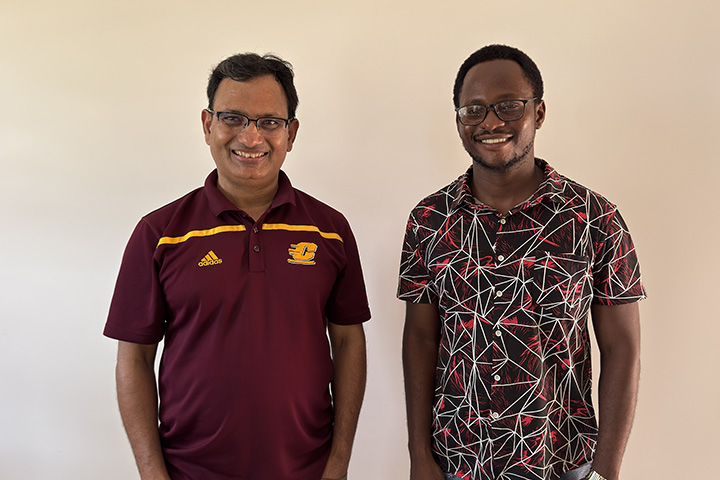 Prakash Adhikari wearing a maroon Central Michigan University shirt stands next to Ernest Pondani wearing a red and white patterned shirt.