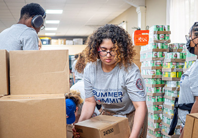 Student moving a box with stacks of canned food and other students nearby