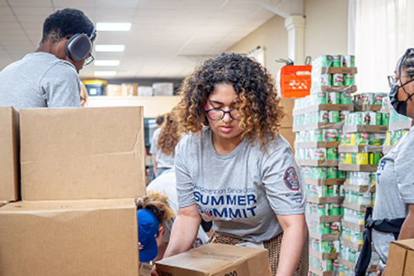 Student moving a box with stacks of canned food and other students nearby