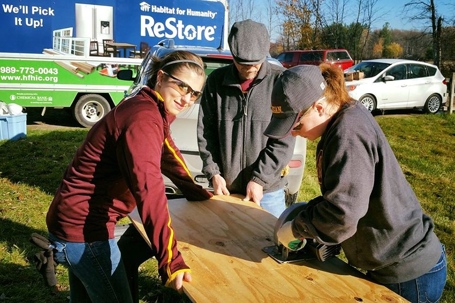 Central Michigan University students cut a large wooden board during a service project with Habitat for Humanity.