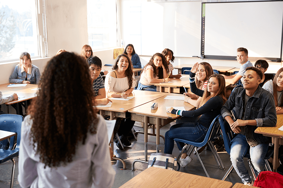 A teacher standing in front of a classroom that is full of students who are all sitting at desks.