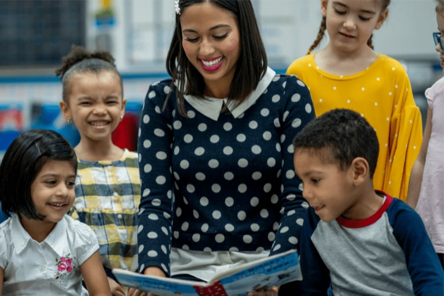 A teacher sits down with her young students and reads a book to everyone.
