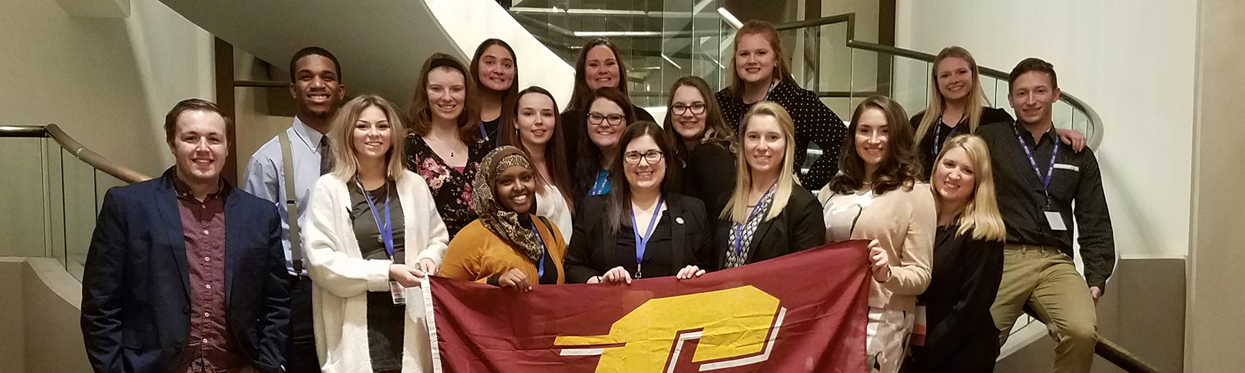 Students hold a CMU flag while standing on stairs during Alliance Management Institute Conference.