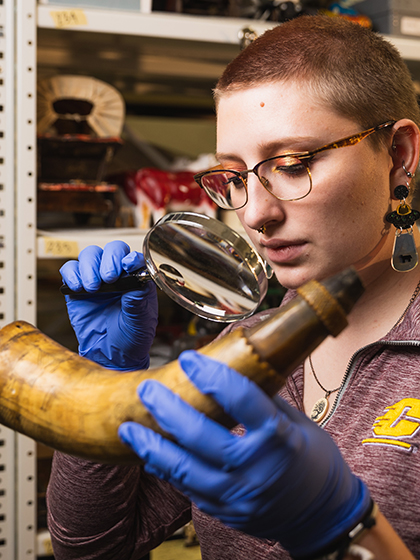 Female museum studies student examines artifact with magnifying glass