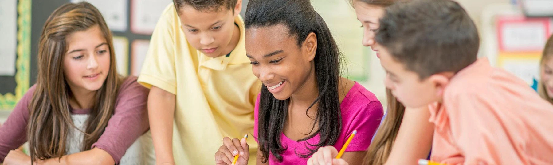 A group of young students at a table, holding pencils, and working on an assignment together.