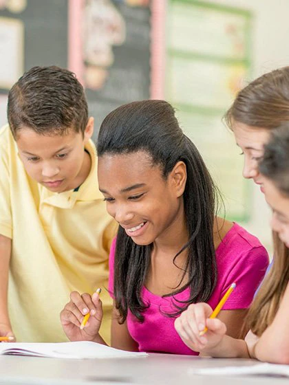 A group of young students at a table, holding pencils, and working on an assignment together.