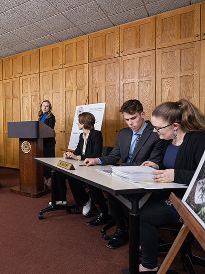 Students seated at table representing the plaintiff review printed materials during a mock trial presentation.