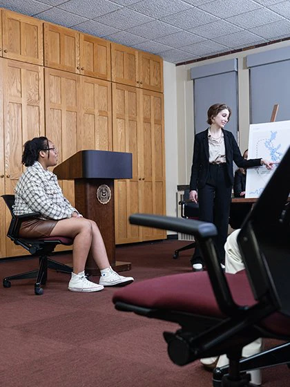 Student standing near a large printed map questions a witness during a mock trial presentation.