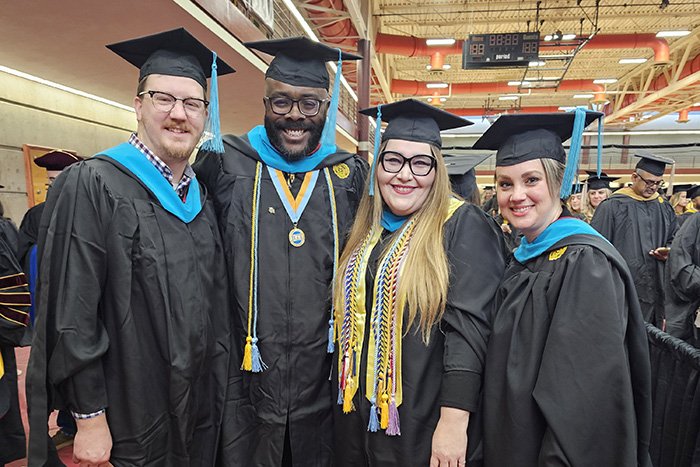 Four Master of Public Administration (MPA) students stand together wearing graduation caps & gowns.