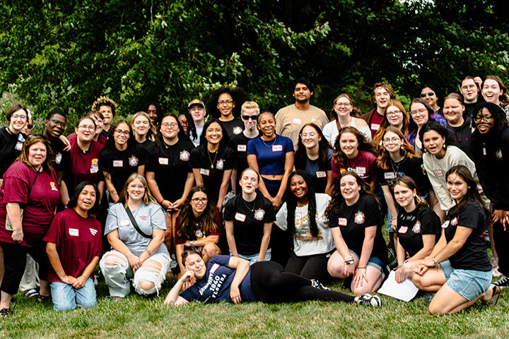 Rows of students from the Public Service Residential College wearing name tags and gather in front of trees to pose for a photo