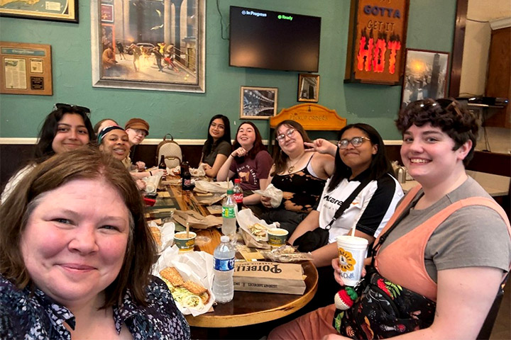 Individuals seated at a table with food and drinks in front of them take a selfie